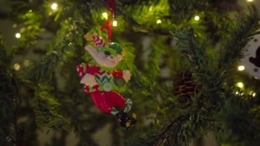 Süslü bir ağaca asılmış neşeli bir Noel elfi. Parlak renkleri ve şenlik detayları, tatil sezonunun neşesini kutlamak için sahneye biraz sihir ve gelenek katıyor..