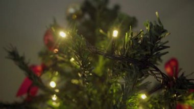 Parlak süslemelerle süslenmiş bir Noel ağacının yakın çekimi, sıcak ışıklar ve sezonun ruhunu yakalayan şenlikli detaylar. Toplar, yaylar ve temalı elementlerin birleşimi.
