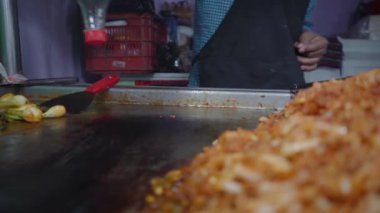 Taco makinesinin elleri ızgaraya yağ ekliyor ve et al pastor pişirmeye hazırlanıyor. Sahne yemek pişirme sürecinin başlangıcını yansıtıyor, Meksika yemeği geleneğini vurguluyor..