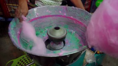 Bir panayırda pamuk şeker yapmak, adım adım şekerin değirmene nasıl döküldüğünü göstermek, renkler ekleniyor ve tatlı iplikler bir çubuğun etrafında şekilleniyor.