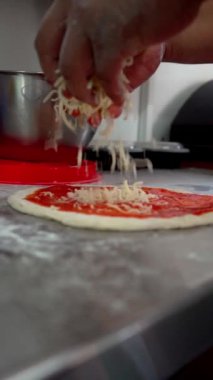 Eller, taze pizza hamurunun üzerine doğranmış mozzarella peynirini eşit bir şekilde yayar. Lezzetli bir yemek için mükemmel bir temel oluşturur. Peynir kremsi dokusu ve parlak rengiyle fırında erimeye hazır bir şekilde patlar..