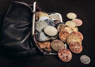 Eski moda deri bir çanta dolusu bozuk para ve etrafa saçılmış. Yan görünüm.