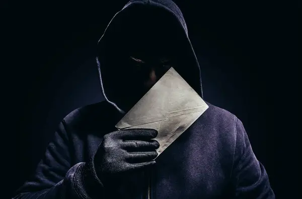 暗い背景に紙の手紙を保持する怖い影のフード付き男の写真 — ストック写真