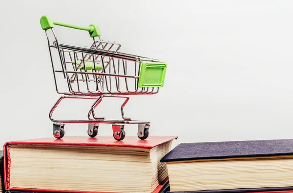 Photo of shopping cart standing on books on white background. Book store concept.