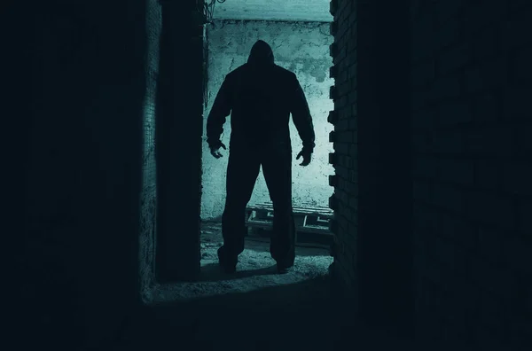 在黑暗的废弃建筑里 一个戴着黑色头巾的男人 跟踪者或杀手站在门口的恐怖照片 图库图片