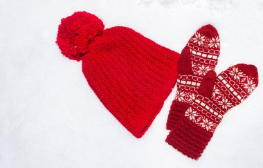 Kar üzerinde örülmüş kırmızı renkli şapka ve kış desenli eldivenlerin fotoğrafı..