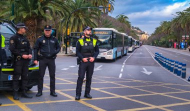 Yol kenarında duran üç polis memuru. Yansıtıcı unsurlara sahip koyu renk üniformalar giyiyorlar ve genellikle kolluk kuvvetleri giysilerinde görülen işaretler var. Subaylardan biri...