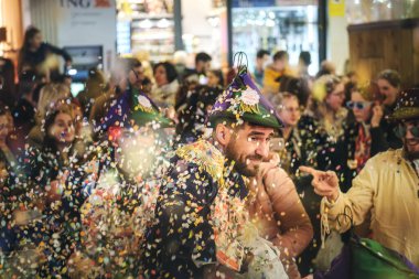 İnsanların bir festivalde ya da karnavalda kutlama yaptıkları canlı bir sahne. Bir sürü renk ve deseni olan şenlikli şapkalar ve kostümler giyiyorlar. Havada konfeti var, neşeli bir olay.