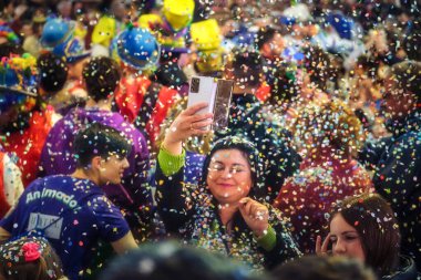 Renkli şapkalar giyen bir sürü insan kutlama yapıyor. Neşeli bir atmosfer var, havada konfeti, festival, parti, ya da halka açık bir kutlama. Selfie ya da fotoğraf çeken biri.