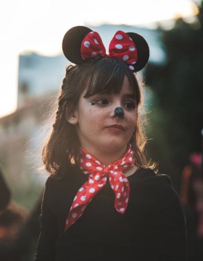 The image shows a child dressed in a costume that includes what looks like Mouse ears, commonly associated with the iconic Disney character Minnie Mouse. The child appears to have a red bow with white clipart