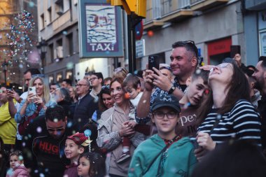 Bir şehir caddesinde şenliğin tadını çıkaran çeşitli kalabalık, yüzen kabarcıklar arasında hareketli anları yakalıyor..