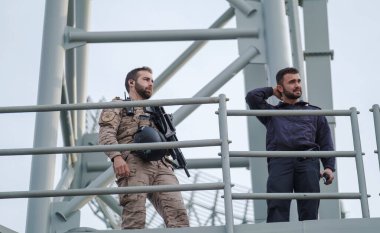 İspanya Malaga 128 2024 Metal bir platformda iki adam, silahlı askeri üniformalı bir adam, güvenlik ya da gözetim durumu öneriyor. Endüstriyel ortam belirsizlik katıyor