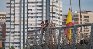 İspanya Malaga 128 2024 Çitin üzerinde İspanyol bayrağıyla kamuflajlı iki askeri şahıs.