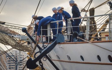 İspanya Malaga 128 2024 Mavi üniformalı denizciler hareketli bir şehir limanında demirlemiş büyük bir gemiyle deniz yolculuğuna hazırlanıyorlar.