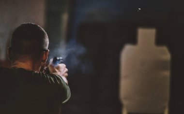 Görüntü, atış poligonunda ateş eden birini gösteriyor. Kişi hedef silueti hedef alıyor. Silahın yanında gözle görülür bir duman var, muhtemelen yakın zamanda ateş edilmiş. Görüntünün açısı