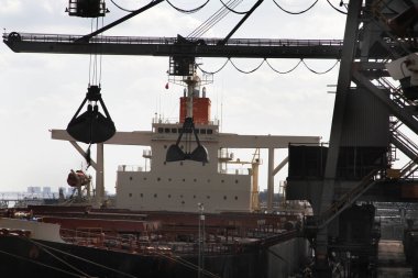 Large bulk transport ship being unloaded at a jetty. clipart