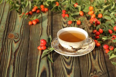 Cup of tea with rose berries on a wooden background