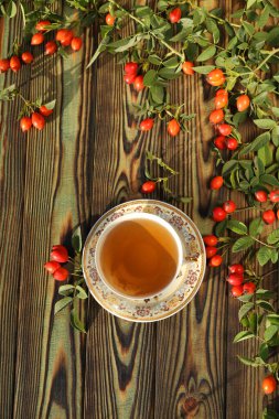Cup of tea with rose berries on a wooden background