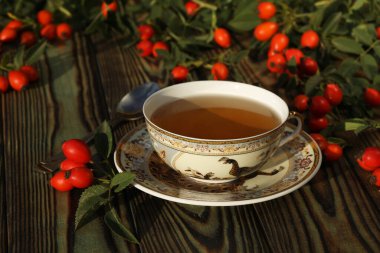 Cup of tea with rose berries on a wooden background