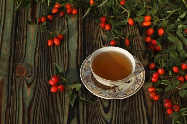 Cup of tea with rose berries on a wooden background