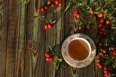 Cup of tea with rose berries on a wooden background