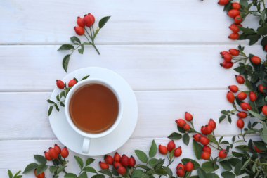 Cup of tea with rose berries on a white wooden background