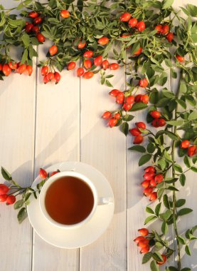 Cup of tea with rose berries on a white wooden background