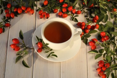 Cup of tea with rose berries on a white wooden background
