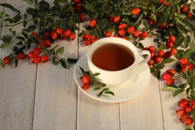 Cup of tea with rose berries on a white wooden background