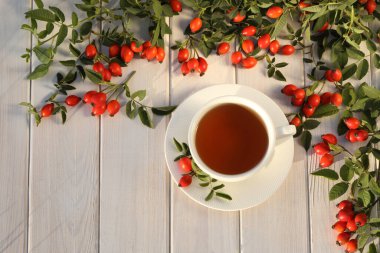Cup of tea with rose berries on a white wooden background
