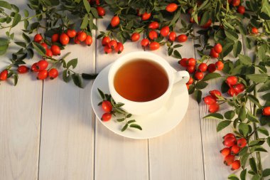 Cup of tea with rose berries on a white wooden background