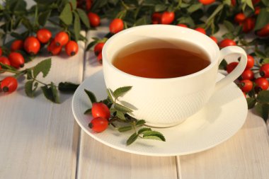 Cup of tea with rose berries on a white wooden background