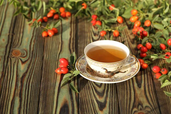 Cup of tea with rose berries on a wooden background