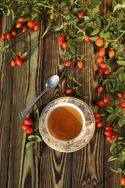 Cup of tea with rose berries on a wooden background