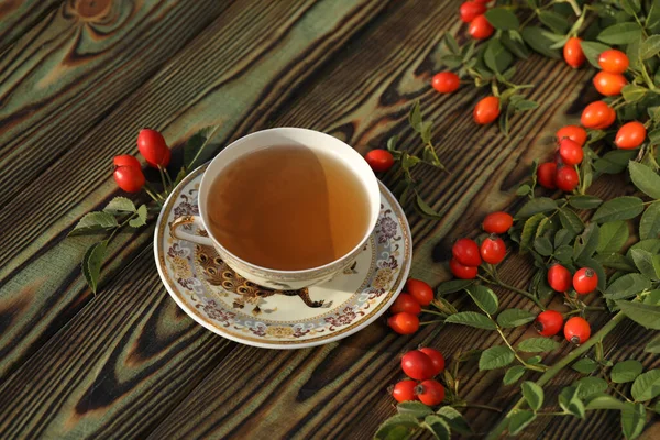 Cup of tea with rose berries on a wooden background