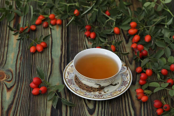 Cup of tea with rose berries on a wooden background