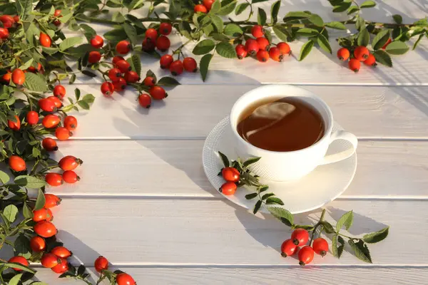 Cup of tea with rose berries on a white wooden background