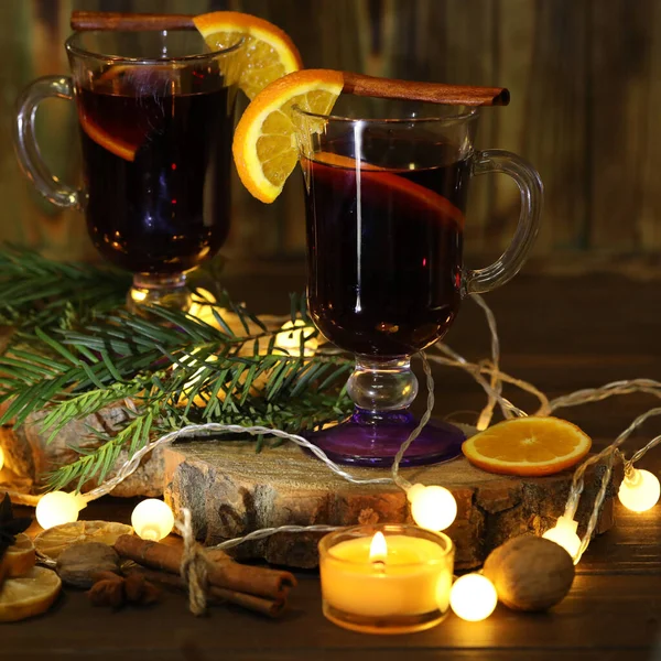 mug of mulled wine with decoration and candles on dark wooden background