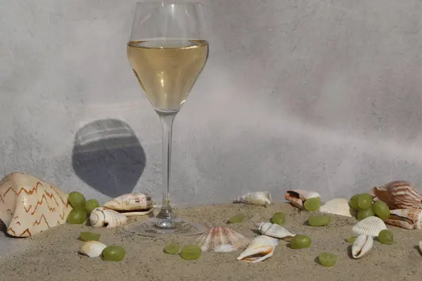 glass of white wine on sand as background with shells