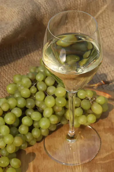 glass of white wine on wooden background with autumn leaves and grape