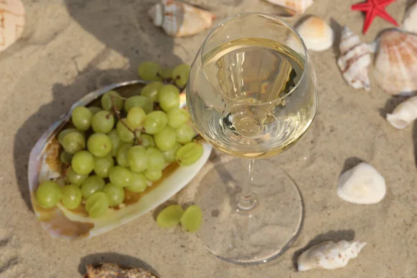 glass of white wine on sand as background with shells