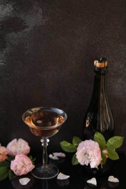 Siyah arka planda gül çiçekleri olan bir bardak pembe şampanya.