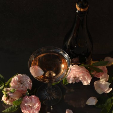 Siyah arka planda gül çiçekleri olan bir bardak pembe şampanya.
