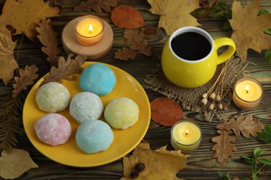 Renkli Japon tatlıları daifuku veya mochi. Tatlılar, sonbahar yaprakları arka planda mumlar ve kahveyle tabağa kapanır.