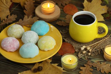 Renkli Japon tatlıları daifuku veya mochi. Tatlılar, sonbahar yaprakları arka planda mumlar ve kahveyle tabağa kapanır.