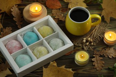 Renkli Japon tatlıları daifuku veya mochi. Tatlılar, sonbahar yaprakları arka planda mumlar ve kahveyle tabağa kapanır.