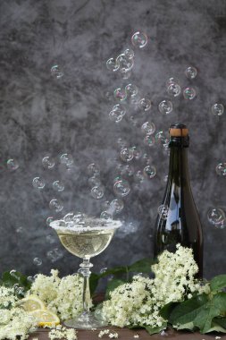 Elderflower likörüyle birlikte bardak ve bir şişe şampanya. Kabarcıklı gri arkaplanda