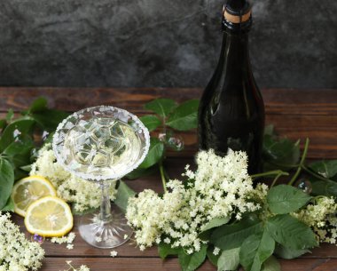 Elderflower likörüyle bir bardak şampanya. Doğal arka planda beyaz yaşlı çiçeklerle süslenmiş.