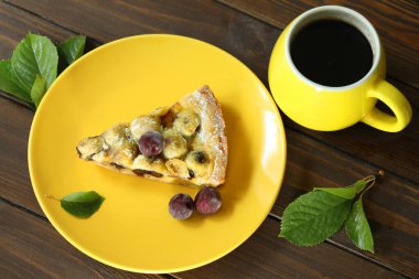 Sarı tabakta vişneli kirazlı lezzetli Quiche turtası ve bir fincan kahve.