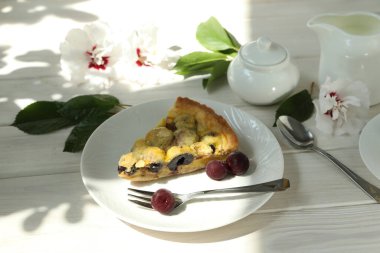 Kirazlı lezzetli Quiche turtası beyaz tabakta bir fincan kahveyle doluyor. Beyaz tahta arkaplan